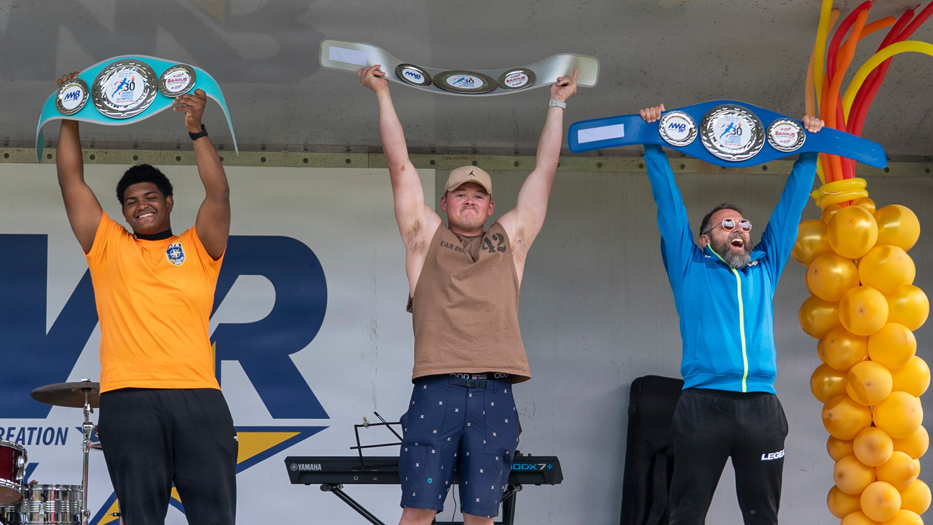 First-, second- and third-place winners stand onstage holding their championship wrestling-style belts overhead at the 30th Annual Armed Forces Olympics at NSA Naples.